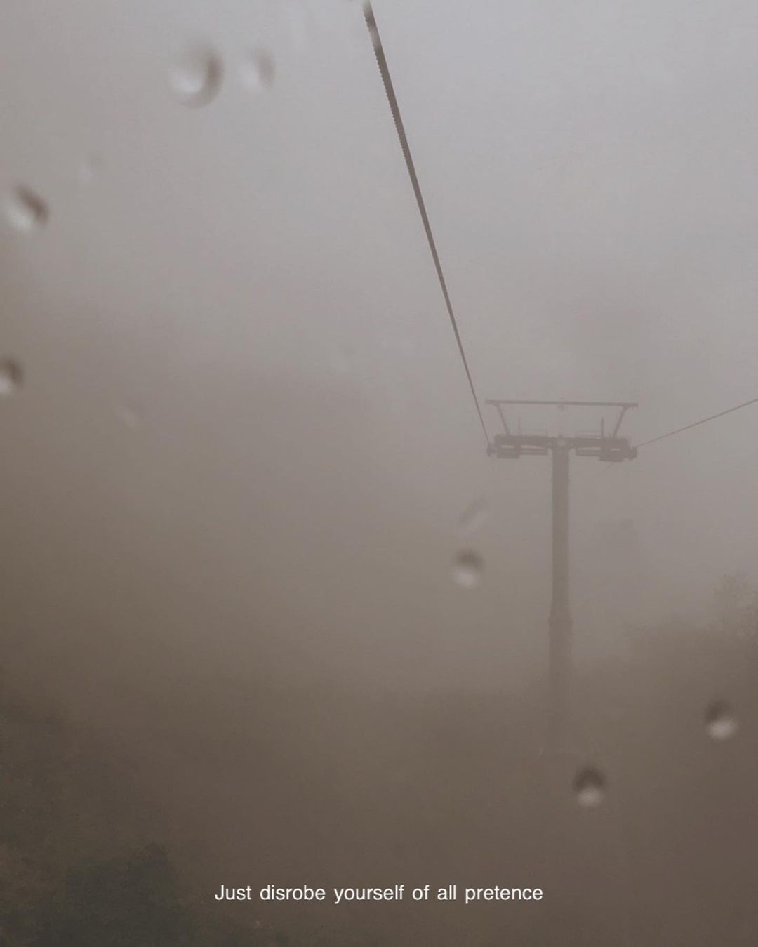 A chairlift pylon disappearing into fog behind a rain-streaked window